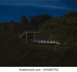 View of train moving under bridge  in mountain area late in the evening; dark blue sky in background