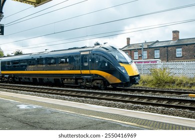 A view from a train station platform as a passenger train flies past at high speed.