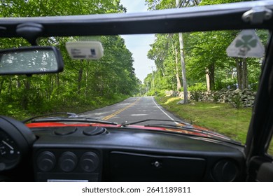 Vista de un camino bordeado de árboles con una pared de piedra desde un convertible Alfa Romeo Spider