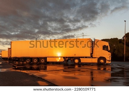 View of a truck with a refrigerated semi-trailer in a parking lot with the evening sun reflected on the side.