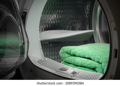 View of the tumble dryer or washing machine with the door open and a green towel inside