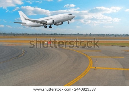 View of the turn from the taxiway onto the runway and a passenger jet plane taking off against the background.