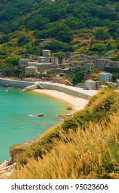 View of turquoise sea and white sand beach at Qinbi village set on a green lush hillside with preserved Fujian style granite beige homes, Mediterranean feel on Beigan, Matsu Islands, Taiwan. Vertical