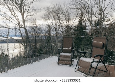 view of two chairs on a balcony with glass barrier on a cloudy day with the forest behind - Shutterstock ID 2283333031