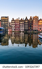 View of typical houses with colorful facades in Amsterdam reflecting in the waters of the canal, and cruise boats