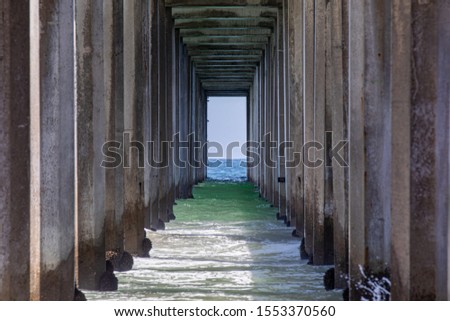 View from under the pier towards the ocean, with support concrete beams on the side. View of the ocean through the portal