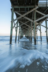 The View Underneath A Old Rustic Wooden Fishing Pier At Sunset. Long Exposure Photo.