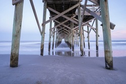 The View Underneath An Old Rustic Wooden Fishing Pier At Sunset. Long Exposure Photo.