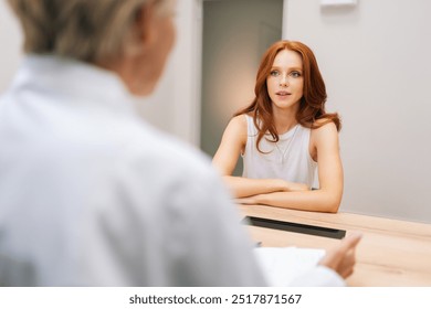 View from unrecognizable therapist shoulder to medical female visitor listening therapist at healthcare appointment. Attractive young woman sitting in modern clinic. Female discussing health treatment - Powered by Shutterstock