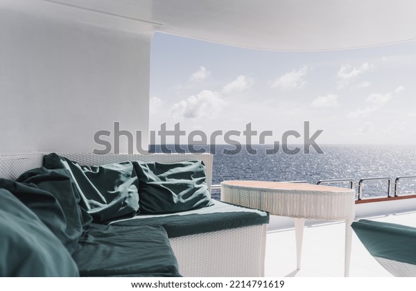 View from the upper deck of a luxurious diving\
safari yacht with a wicker table and a sofa with teal cushions on\
it, and an ocean horizon with a bright sparse cloudscape in a\
defocused background