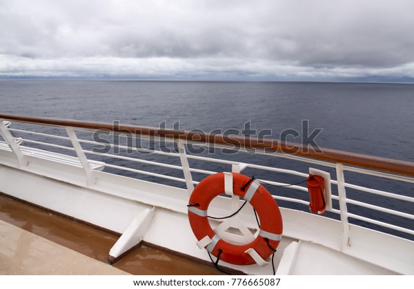 View\
from upper deck of modern cruise ship showing lifesaver ring and\
teak railings on a grey stormy day in the\
Tropics.