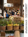 View of urban farmers market with baskets of vibrant vegetables in the foreground and people in the background.