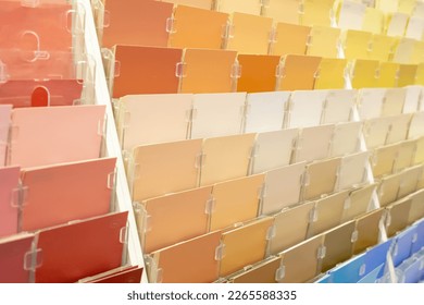 A view of a variety of warm color shade paper samples, seen on a rack in the paint department of a local home improvement store.