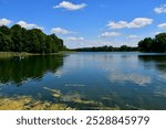 A view of a vast river or lake surrounded from all sides with reeds, forests, moors, fields, and pasturelands located next to a small marina or wooden platform and some metal tower seen in Poland