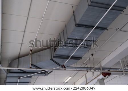 View of ventilation tube hanging on the ceiling and light of a commercial center. Ventilation system, hot and cold air.