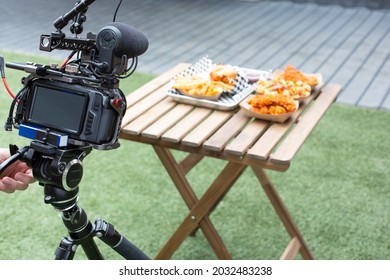 A View Of A Video Camera In Front Of A Patio Table Of American Street Food, In An Outside Patio Setting.