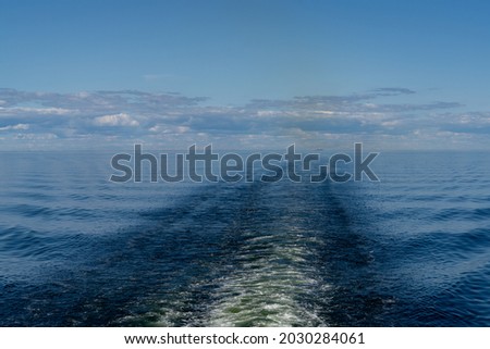 View of the wake of a large ship in the calm open ocean under a blue sky