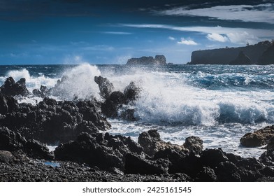 View of waves crushing over black rocks; distant shore in background