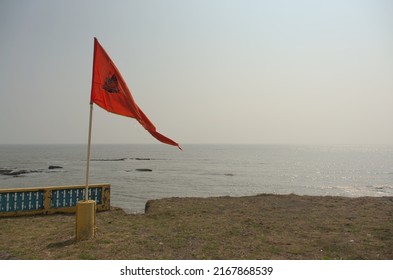 View of a waving saffron flag with emblem of Shiva, a god in Hinduism, on a bright summer day at Gangeshwar Mahadev Temple, a famous tourist place located on the coast of Arabian Sea, Diu, India