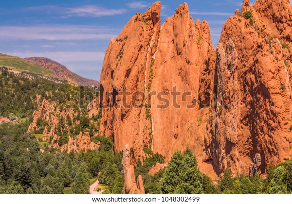 View of whimsical rock formations in the Garden of\
the Gods park, Colorado Springs, Colorado; on the bottom, tiny\
figures of people walking on the ground; parked cars on the left\
side; Colorado, USA