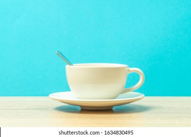 View Of A White Coffee Cup With A Spoon Inside On The Table, Side View, Blue Background