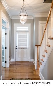 View of a white front door entrance in a new construction house with a hanging chandelier clear glass light and a staircasefrom the interior