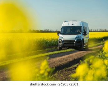 Vista de la camioneta blanca en la carretera de tierra a través de flores amarillas de colza en el día de primavera