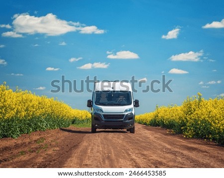 view to white van on ground road between agriculture rapeseed fields under blue sky