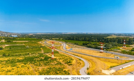 View of winding road and fields on a sunny day in the countryside. A winding road cuts through green fields under a clear blue sky.