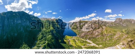 view of a winding road snaking through a stunning Norwegian fjord. Lush green mountains and a deep blue body of water create a breathtaking landscape under a clear blue sky. Lysefjord, Norway