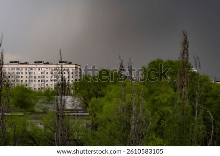 View from the window at the beginning of the evening spring thunderstorm - clouds have gathered, trees are swaying from a strong wind, a piece of the roof has come off on a nearby building.