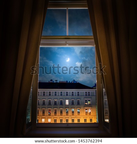 The view from the window of the old night city of Vienna and the moon in the cloudy sky.