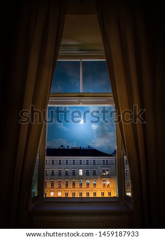 The view from the window of the old night city of Vienna and the moon in the cloudy sky.