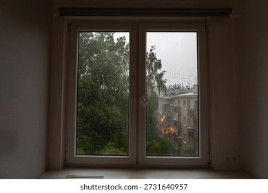 View from a window showing rain falling on buildings and trees in an urban area
