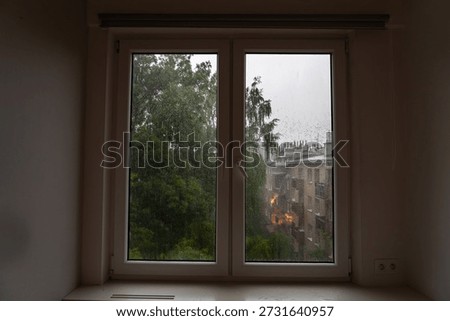 View from a window showing rain falling on buildings and trees in an urban area