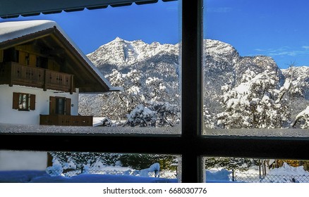 View from the window to the snow-capped Alps and a wooden house in the mountains. - Shutterstock ID 668030776