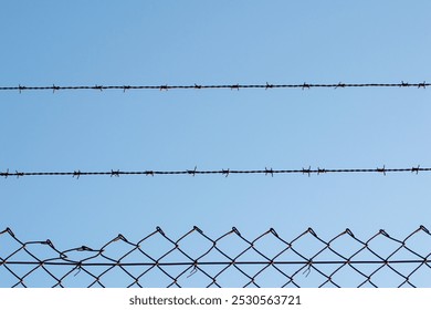 view of a wire fence with barbed wire on top of it on a blue sky day - Powered by Shutterstock