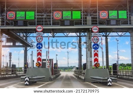 View without cars at the entrance to the toll road, limited by the barrier. Cashless payment transponder, speed limit signs