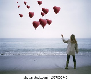 View Of A Woman Letting Heart-shaped Balloons Go On The Beach