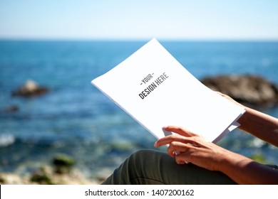 View Of Woman Reading A Magazine By The Sea In The Sun. With Water And A Blue Sky In The Background. Magazine Cover Mockup.