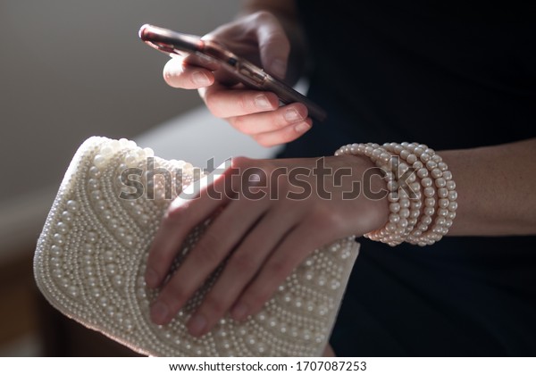 View\
of a woman seated wearing a black dress holding her mobile phone\
cell using it to keep up to date and in contact with people during\
COVID-19 lit by natural light from a nearby window\
