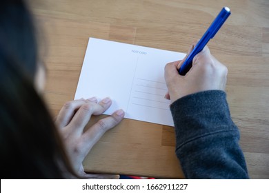 View Of Woman Writing Message On Blank Postcard For Send Back To Home.