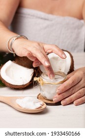 View Of A Woman's Hand Picking Up Coconut Oil From A Glass Jar To Apply It To Her Hair.