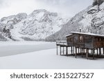 View of a wooden hut overlooking the completely frozen Braies Lake on a snowy winter day; Dolomites, Italy