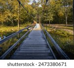 View of wooden suspension bridge in  Midwestern state park with one fisherman on clear fall day