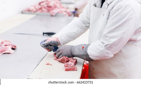 View of a worker in meat factory, chopped a fresh beef meat in pieces on metal work table, industry of a processing and production food. Horizontal view.