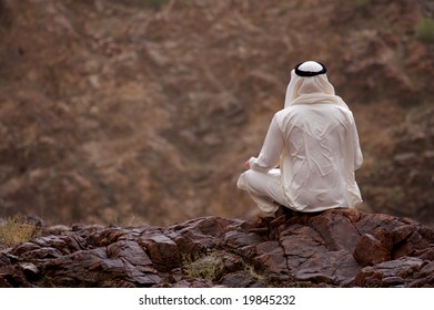 A View Of A Young Arab Man Sitting On A Rocky Overlook.