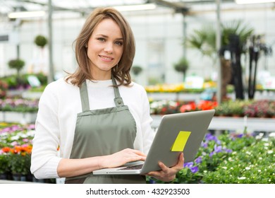 View Of A Young Attractive Woman Working At The Plants Nursery Using Laptop