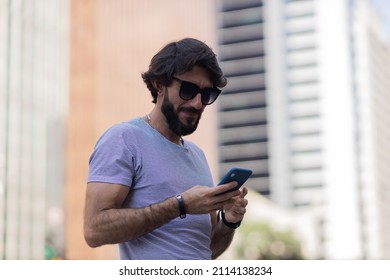 View of young man using a smartphone at day time with city view landscape in the background. Mobile phone, technology, urban concept. High quality photo