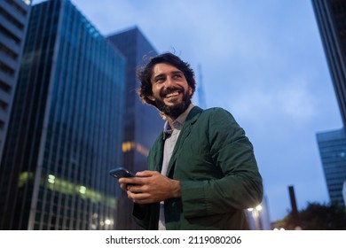 View of young man using a smartphone at night time with city view landscape in the background. Mobile phone, technology, urban concept. High quality photo - Powered by Shutterstock